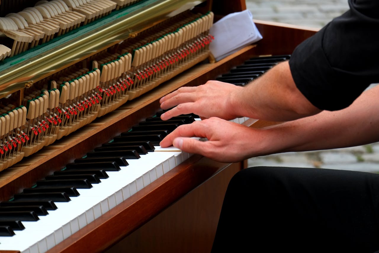 A musician plays an upright piano, showcasing intricate hand movements and exposed piano mechanics.